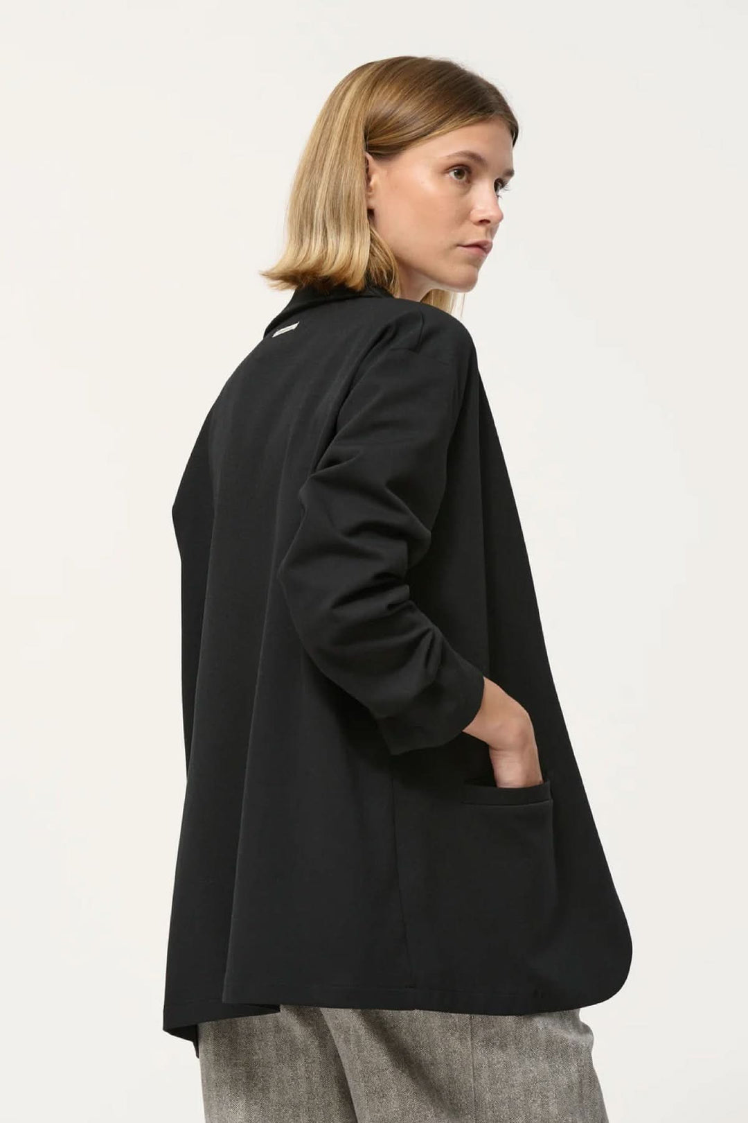 Veston Cayden noir, coupe droite ample, manches longues, fausses poches passepoilées, porté ouvert sur tenue ajustée.