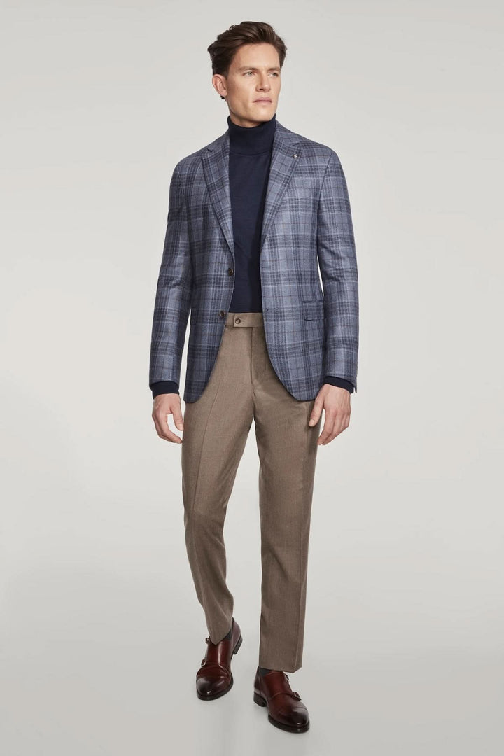 Veste à carreaux en laine et soie portée par un homme avec un pull bleu marine et un pantalon beige.