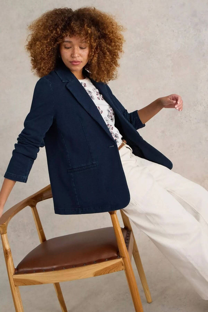 Veston décontracté en denim porté par une femme avec cheveux bouclés, assise sur une chaise en bois.