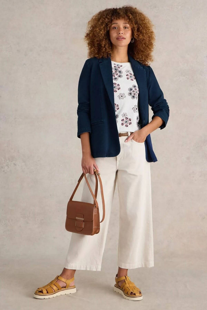 Femme stylée en veston décontracté bleu, t-shirt imprimé, pantalon clair et sac caramel.