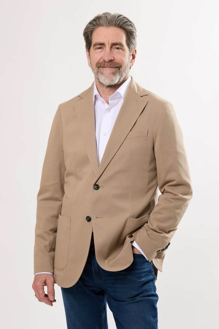 Homme portant un veston en coton extensible beige, alliant style et confort, idéal pour des tenues habillées ou décontractées.