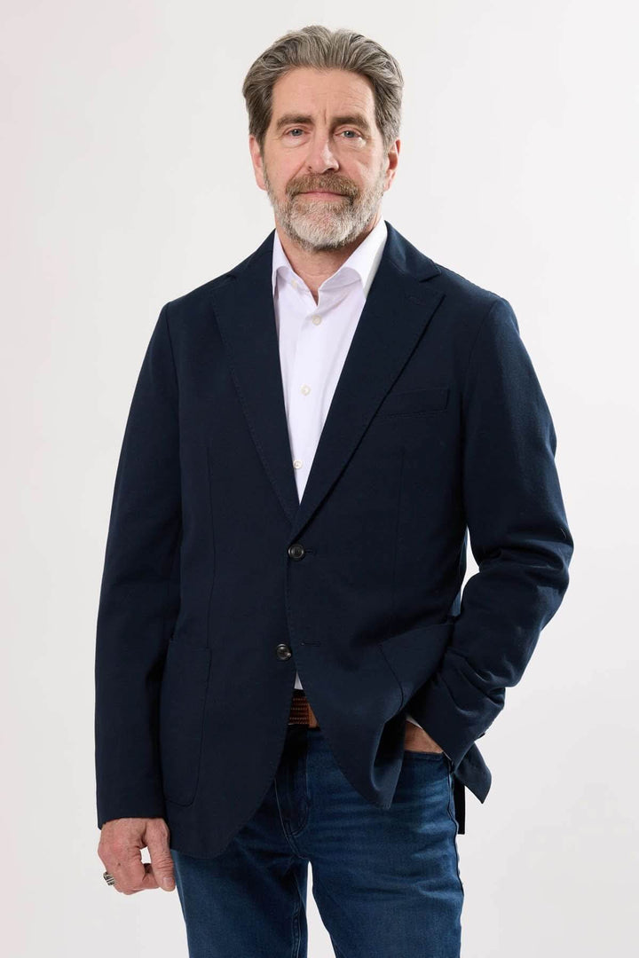 Homme portant un veston en coton extensible, style moderne et décontracté, avec jeans et chemise.