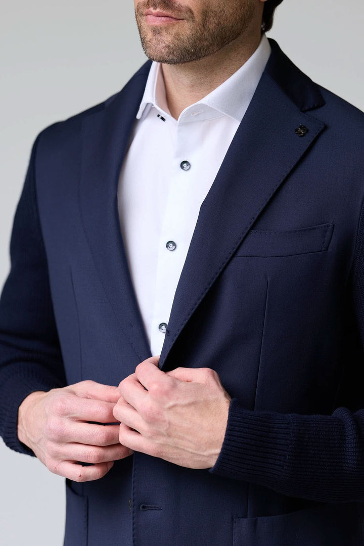 Homme portant un veston hybride tricot et tissu avec manches en maille et col à revers classique, look chic et décontracté.