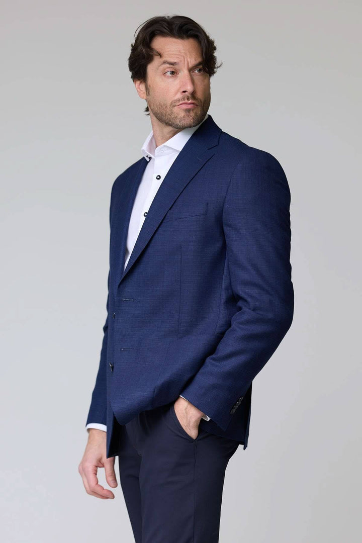 Homme portant un veston structuré à micro motif bleu, élégant et moderne, idéal pour le bureau ou les occasions habillées.