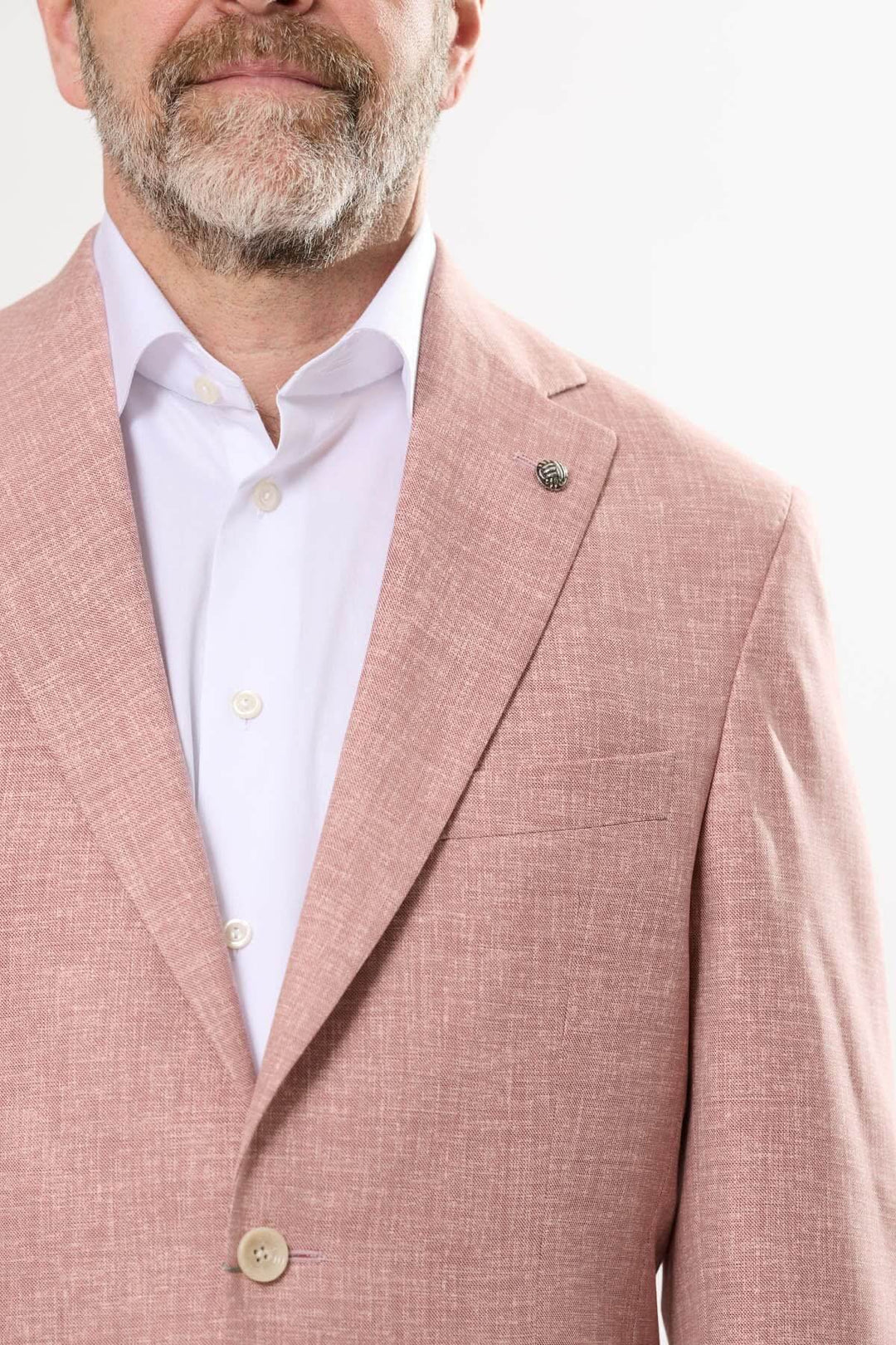 Homme portant un veston texturé rose à coupe moderne, avec une chemise blanche et un bouton ornemental.