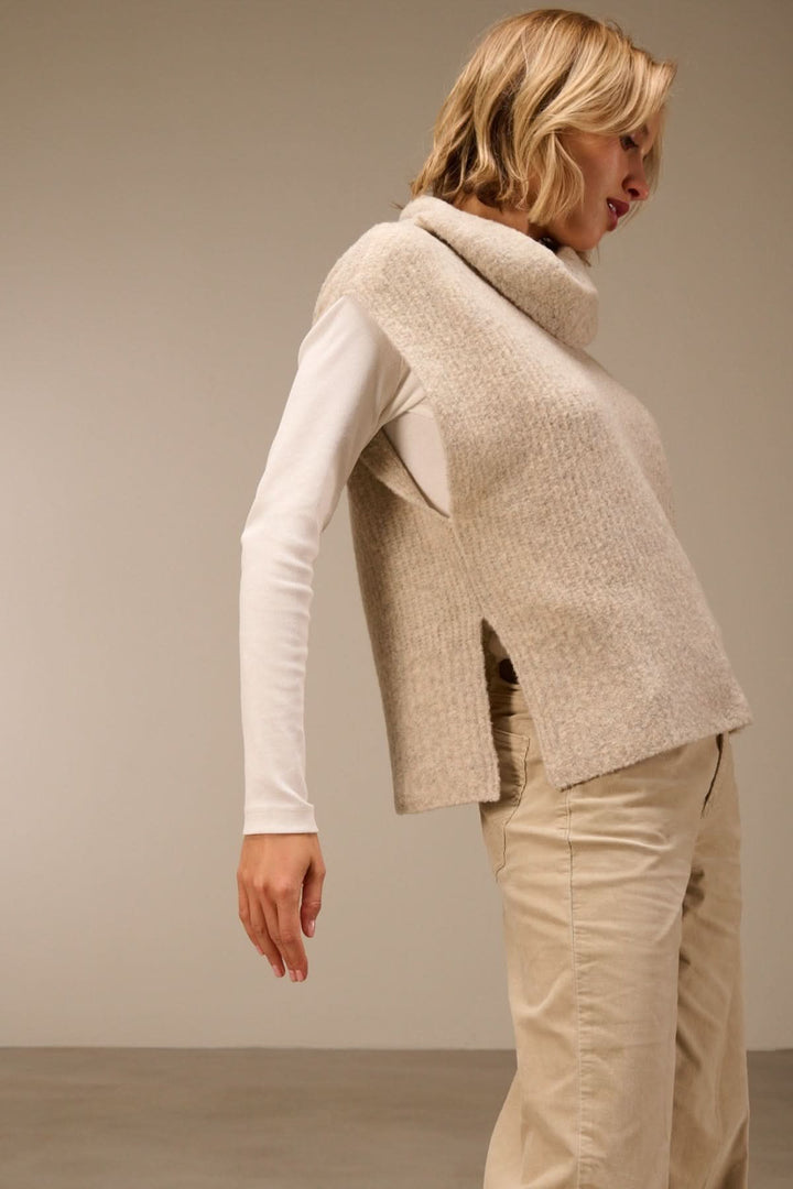 Femme portant un gilet sans manches en maille bouclée à col drapé sur un t-shirt blanc, style élégant et confort.