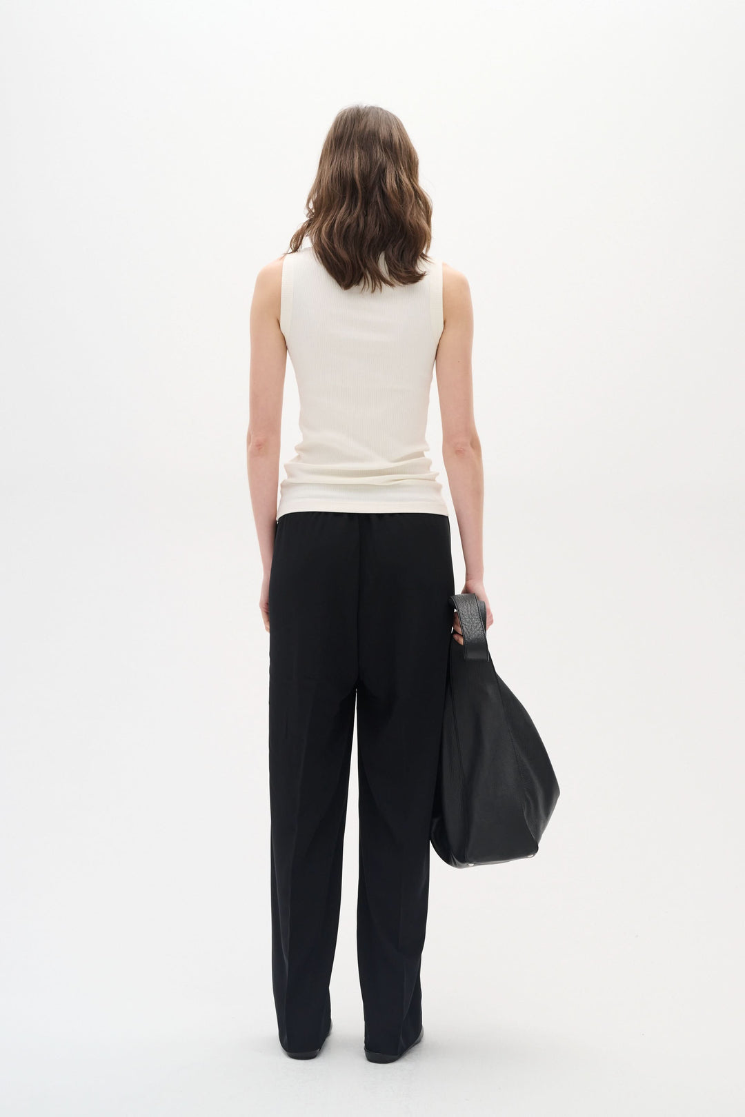 Femme de dos portant une camisole sans manches Dagna beige, avec pantalon noir et sac à main.