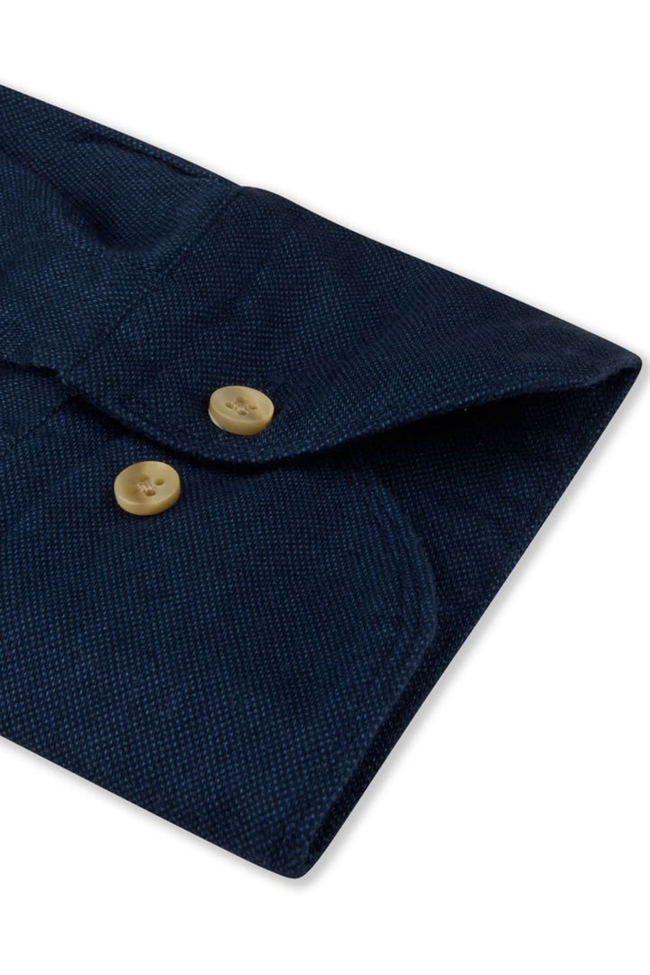 Détail d'une chemise sport en coton, col semi-italien et boutons dorés sur tissu bleu foncé.