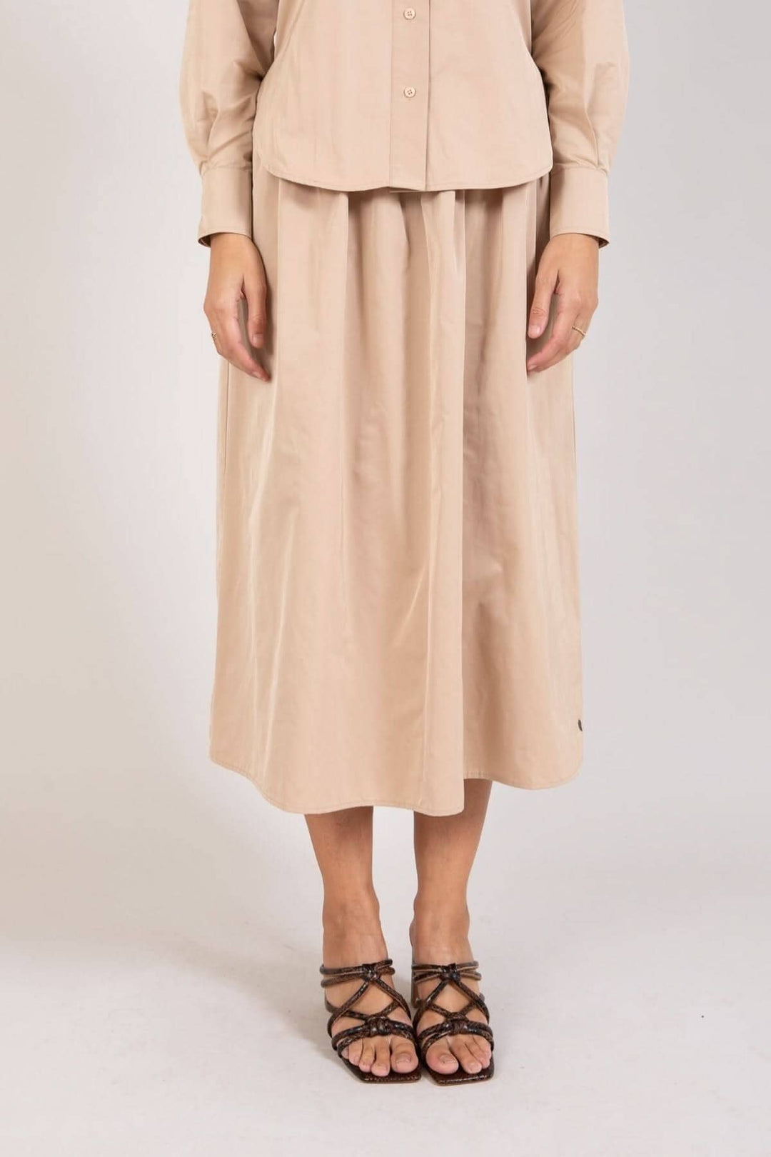 Jupe longue beige avec plis, longueur mollet, portée avec un haut assorti et des sandales élégantes.