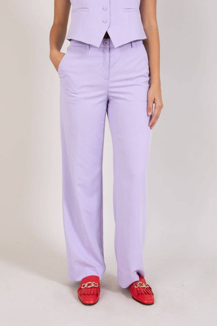 Pantalon à jambes larges lavender porté avec un veste assortie, idéal pour bureau ou événements, avec chaussures rouges.