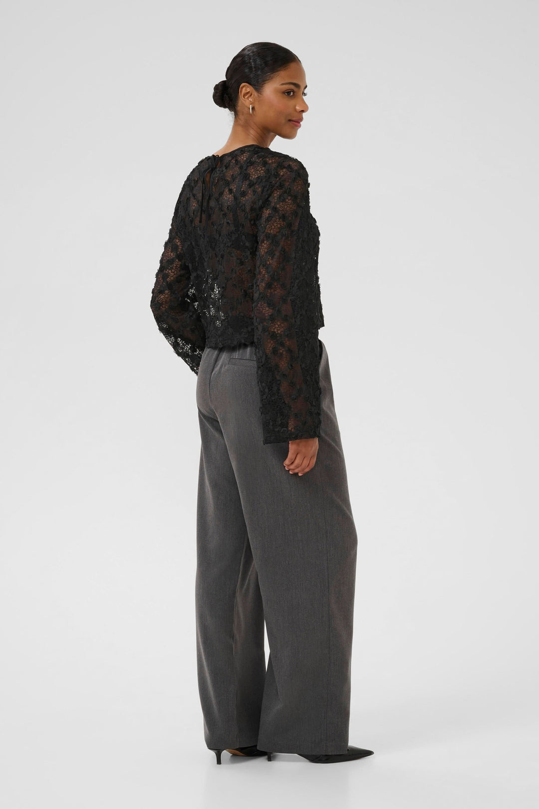 Femme portant la Blouse Rosie en dentelle florale à manches longues avec motifs floraux en relief, vue arrière élégante.