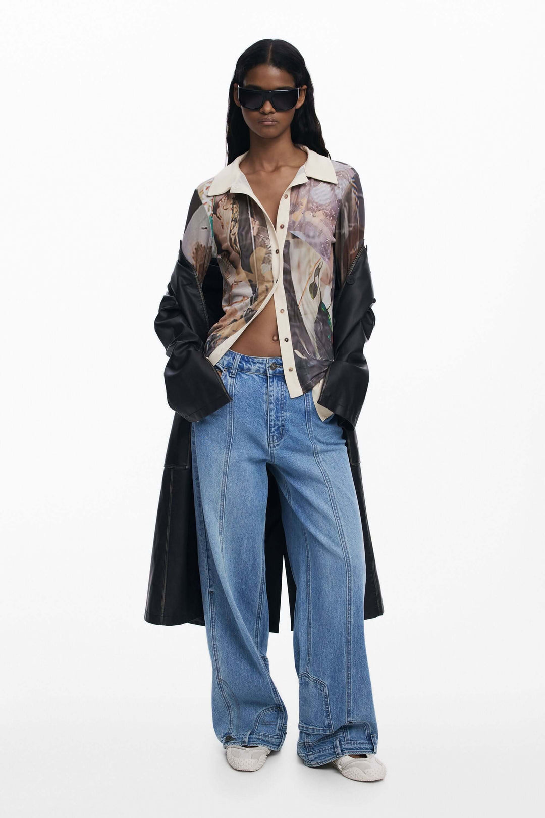 Modèle portant un T-shirt en mousseline avec poignets, aux imprimés artistiques, associé à un jean décontracté et un trench-coat.