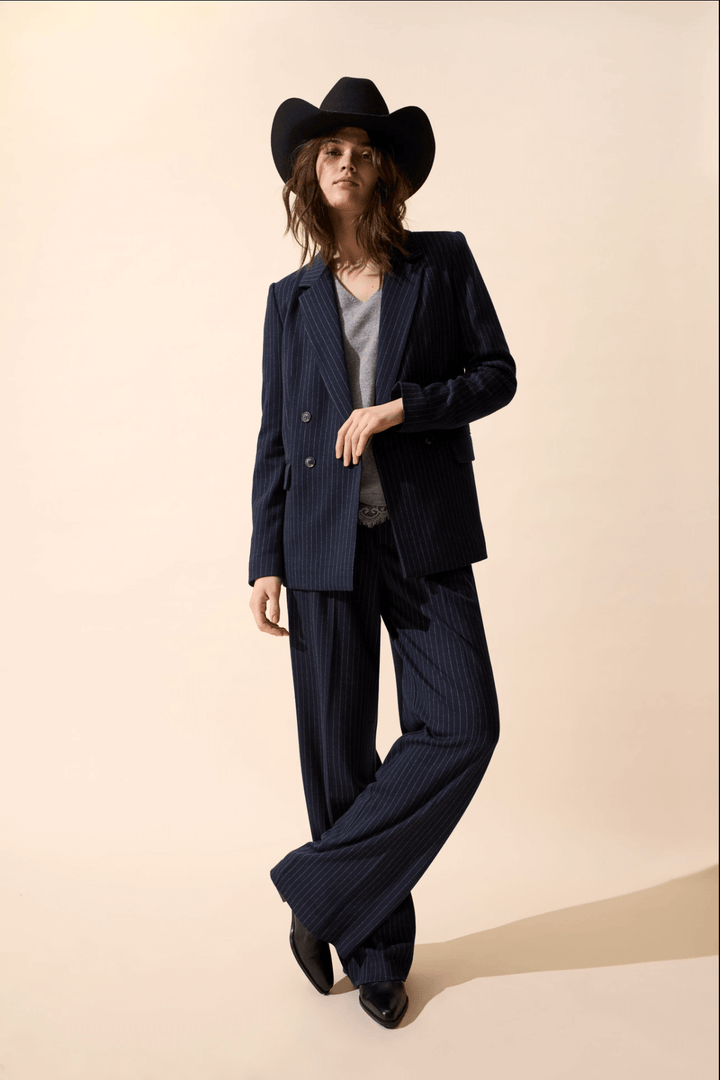 Femme en veston à rayures, pantalon large et chapeau de cowboy, look chic décontracté.