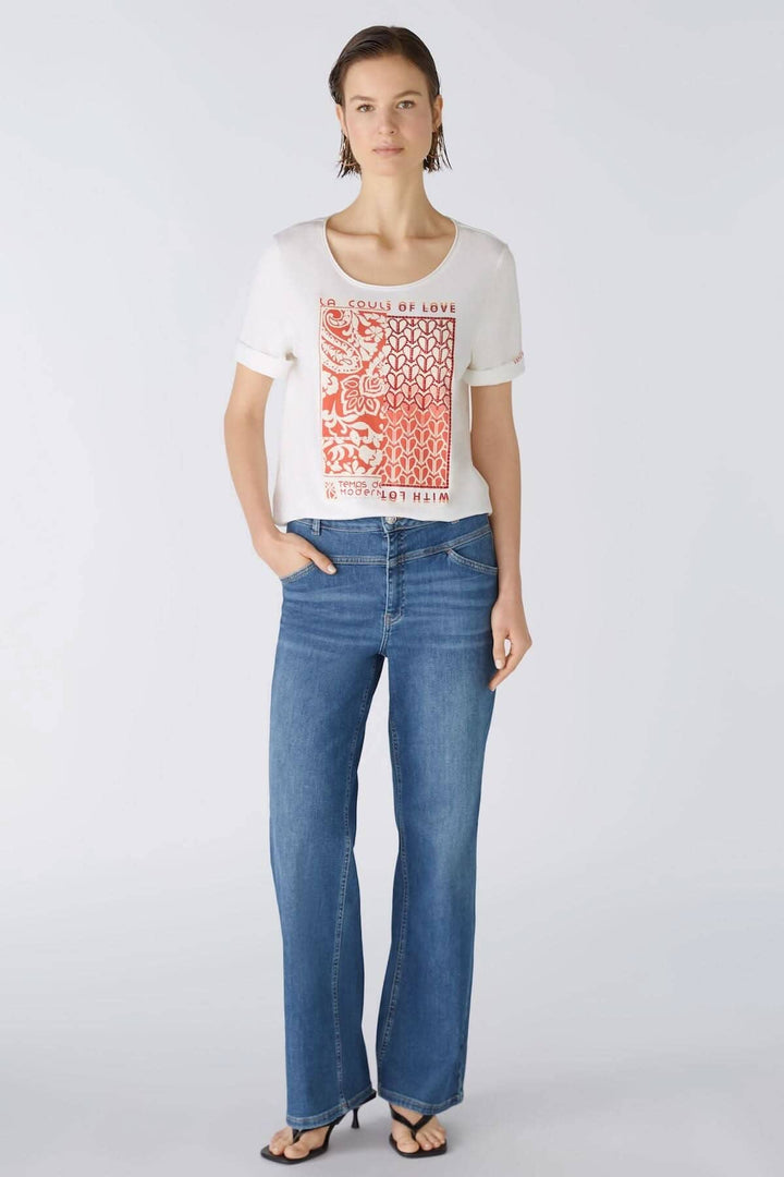 T-shirt avec imprimé graphique rouge, manches courtes, porté avec un jean bleu, style décontracté.