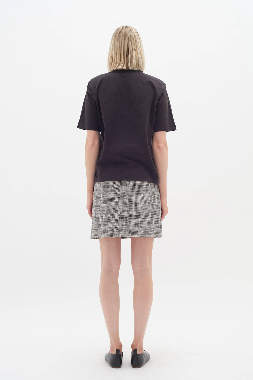 Femme vue de dos portant une jupe Zaccai à motif de carreaux et un t-shirt simple, idéale pour le bureau.