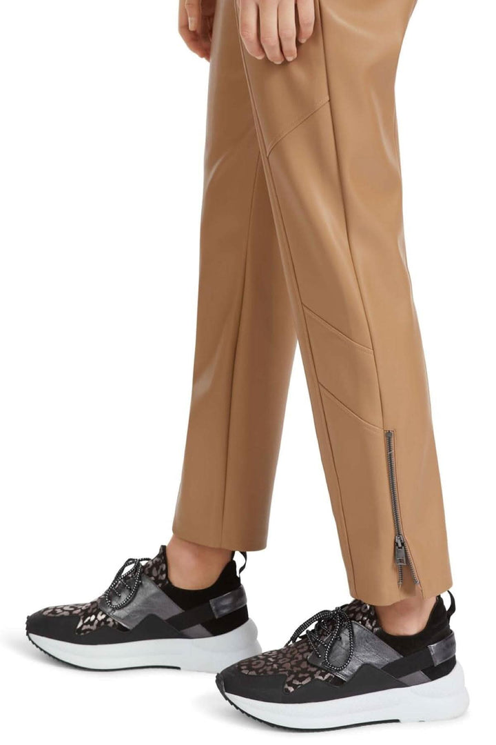 Pantalon en cuir SOFIA beige avec fermeture éclair, associé à des baskets modernes noires et blanches.