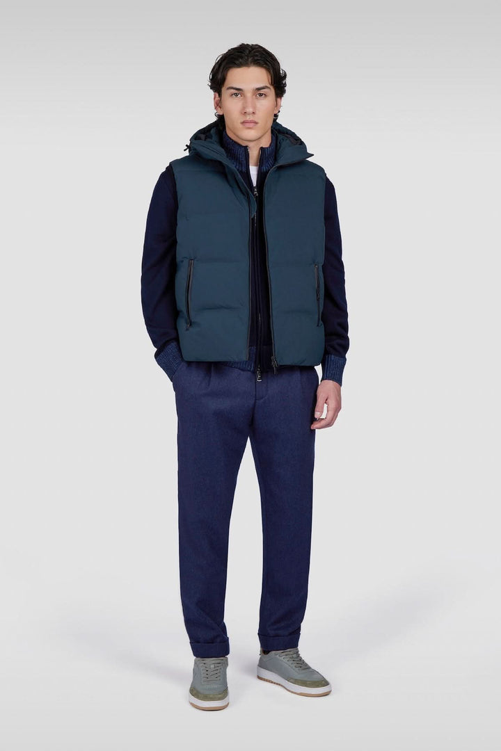 Homme portant un gilet bleu avec capuche, style décontracté, pantalon assorti, look contemporain.