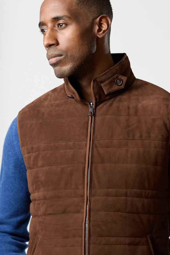 Homme portant une veste sans manches en simili suède, élégante et contemporaine, sur un chandail bleu pour une silhouette structurée.