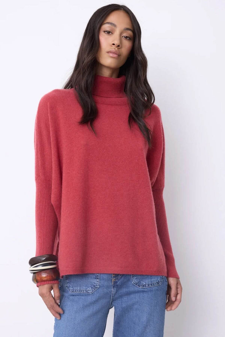 Femme portant chandail à col roulé en cachemire rouge, style élégant et décontracté avec jean, manches longues et coupe ample.