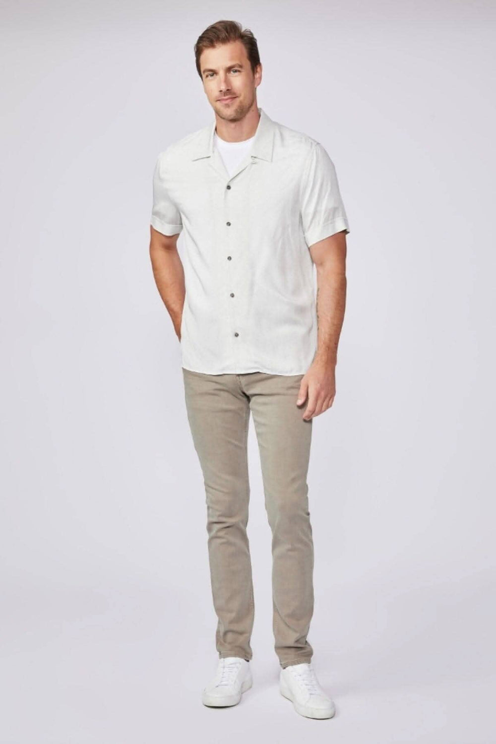 Homme portant une chemise blanche et un jeans beige, style moderne et décontracté.