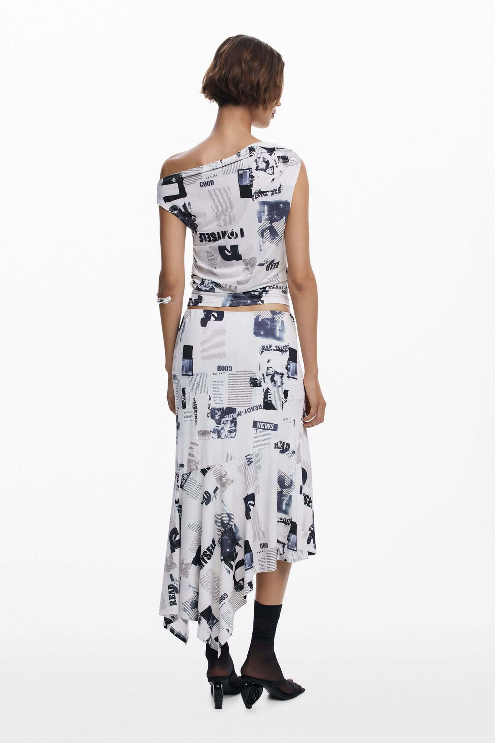 T-shirt drapé asymétrique à col bateau, imprimé typographique contemporain, porté avec jupe à effet drapé.
