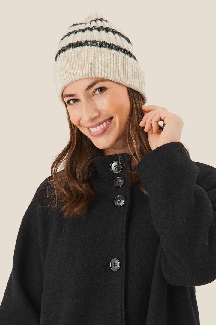 Femme souriante portant un bonnet à rayures grises et blanches, assortie d'un manteau noir.