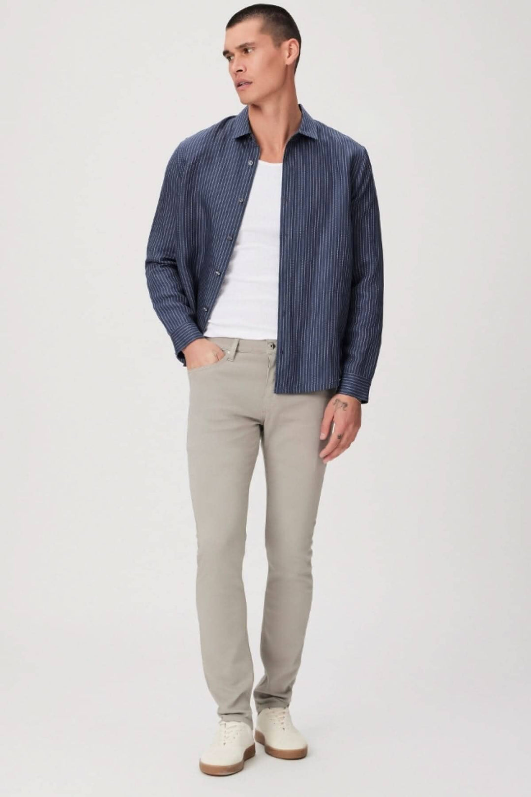 Homme en jean gris clair et chemise rayée bleue, style moderne et décontracté, avec chaussures blanches.