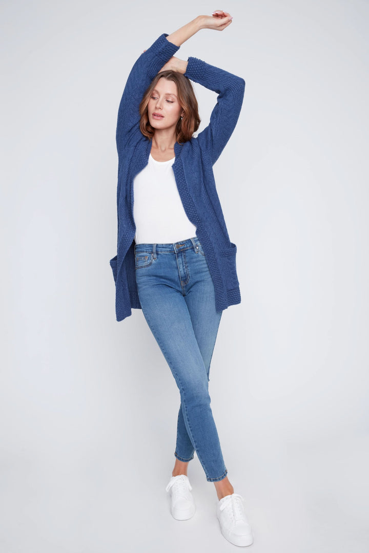 Cardigan long à manches longues en maille torsadée, porté avec un top blanc et un jean, affichant un style cosy.