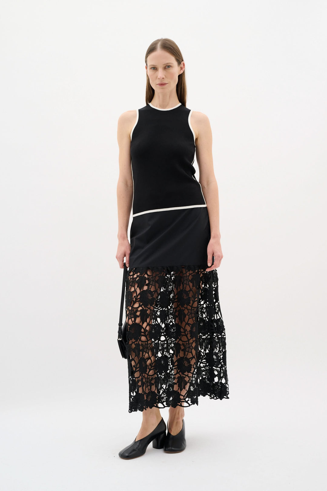 Modèle portant un camisole noir à encolure ronde, associé à une jupe en dentelle noire, look minimaliste et raffiné.