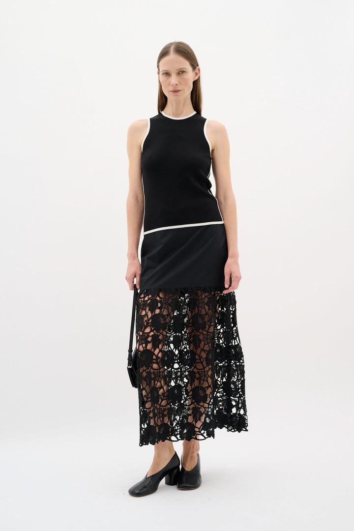 Modèle portant un camisole noir à encolure ronde, associé à une jupe en dentelle noire, look minimaliste et raffiné.