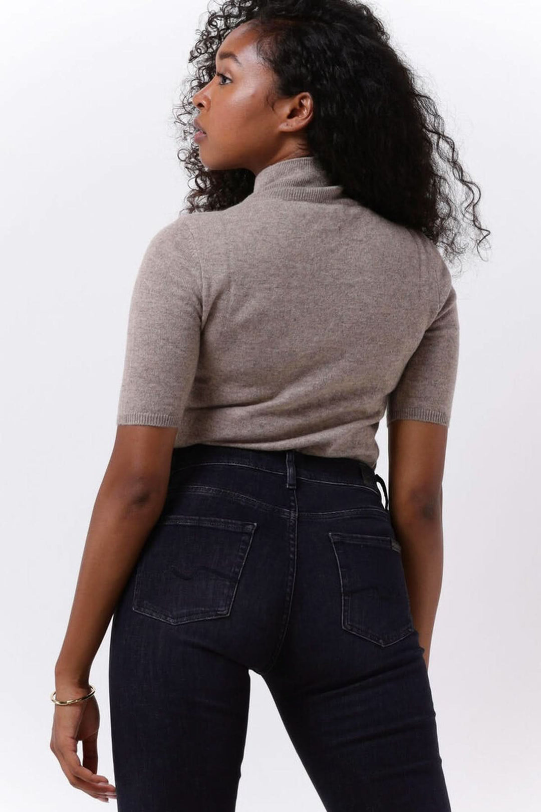 Femme portant un Chandail col montant manches courtes — maille fine, stylé avec un jean foncé pour un look élégant et moderne.