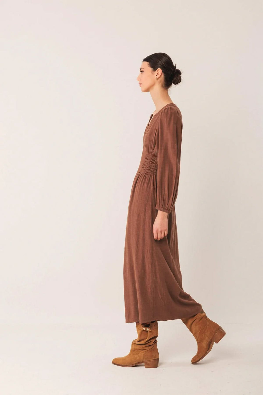 Femme portant une robe longue à encolure V et manches bouffantes, associée à des bottes pour un look chic et décontracté.