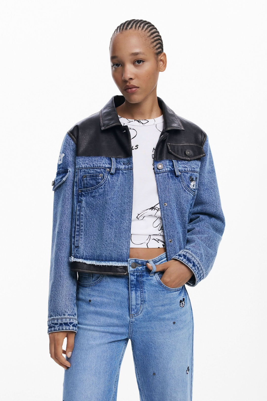 Femme portant une veste en jean stylée avec manches en cuir noir, associée à un t-shirt graphique et un jean décontracté.