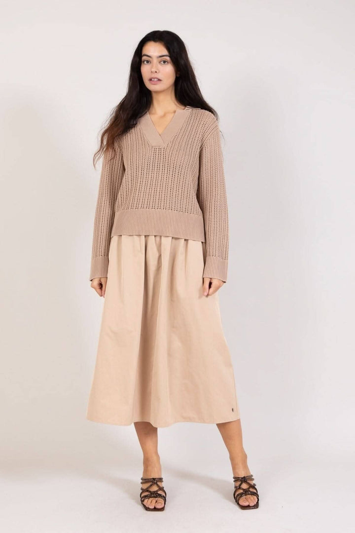 Femme portant un chandail maille ouverte beige avec encolure en V et une jupe longue beige.