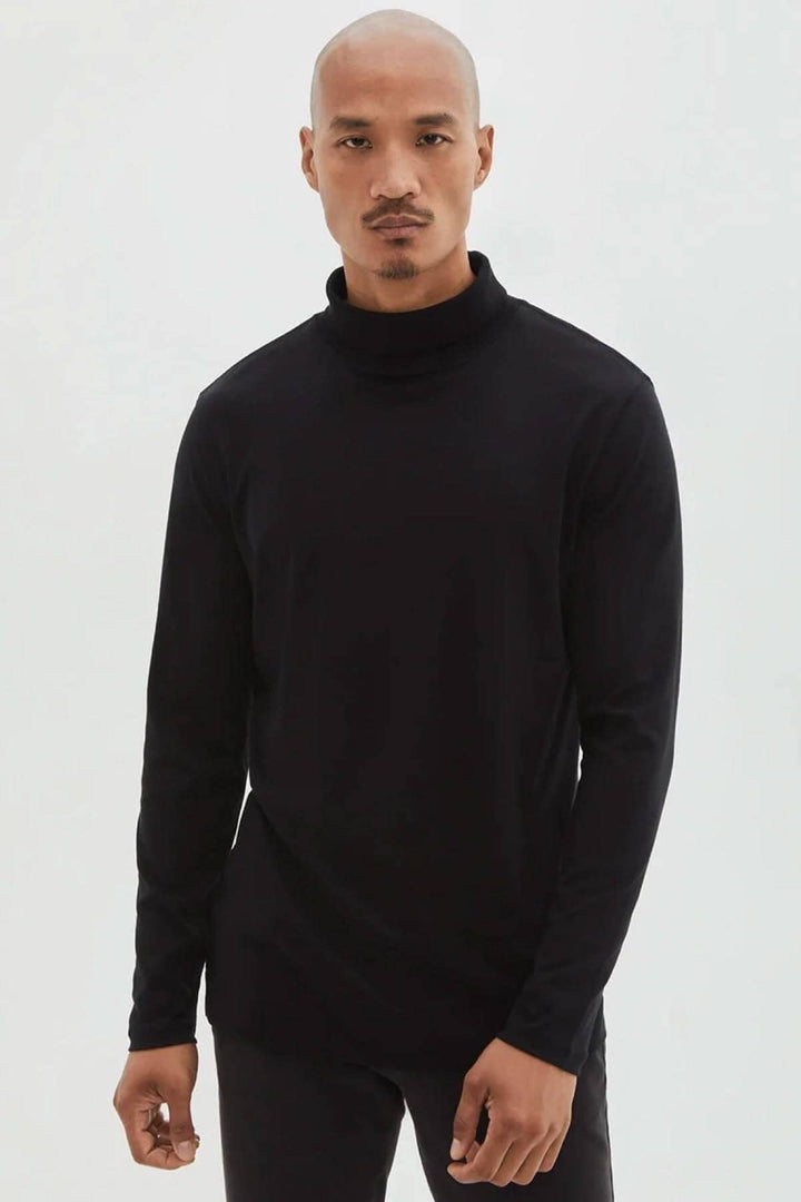 Homme portant un col roulé en coton noir, à manches longues, avec une coupe élégante et moderne.
