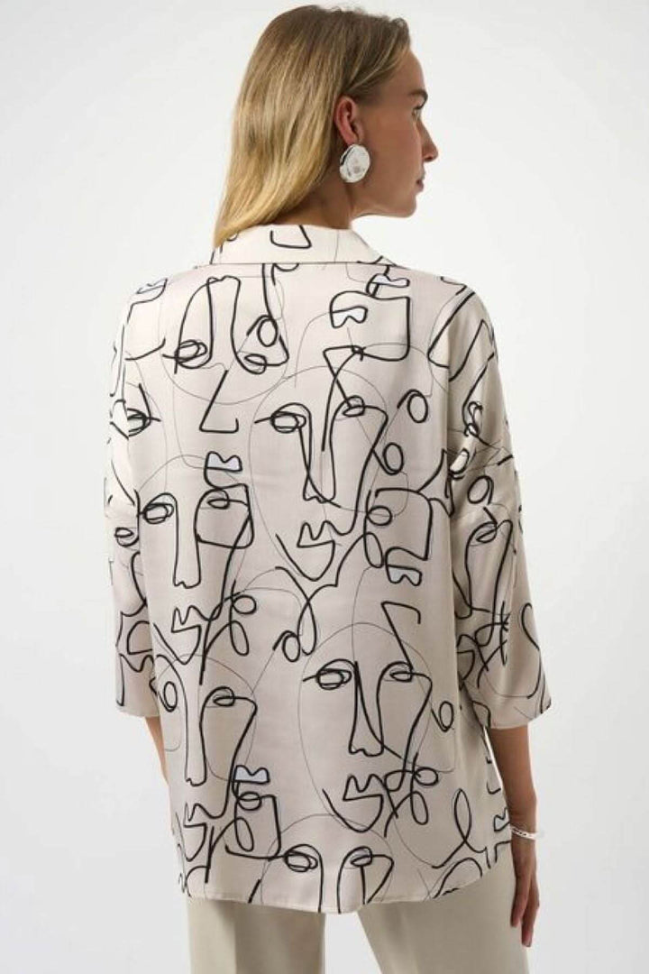 Blouse imprimée graphique avec motifs abstraits de visages, col chemise ouvert et manches mi-longues.