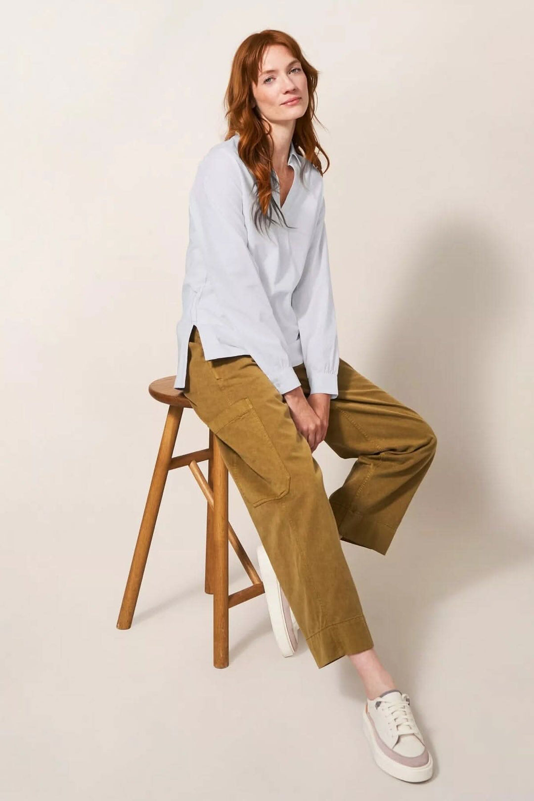 Femme portant une chemise à manches longues encolure V et pantalon en velours côtelé, assise sur une chaise en bois.