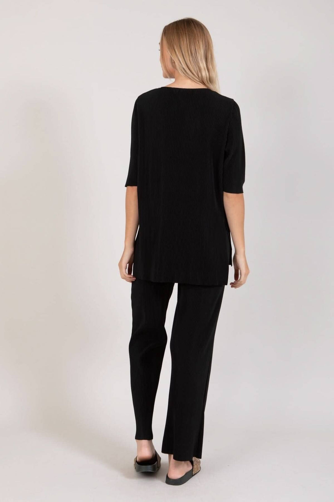 Femme vue de dos portant un ensemble noir chic, comprenant un haut et un pantalon ample avec des poches.