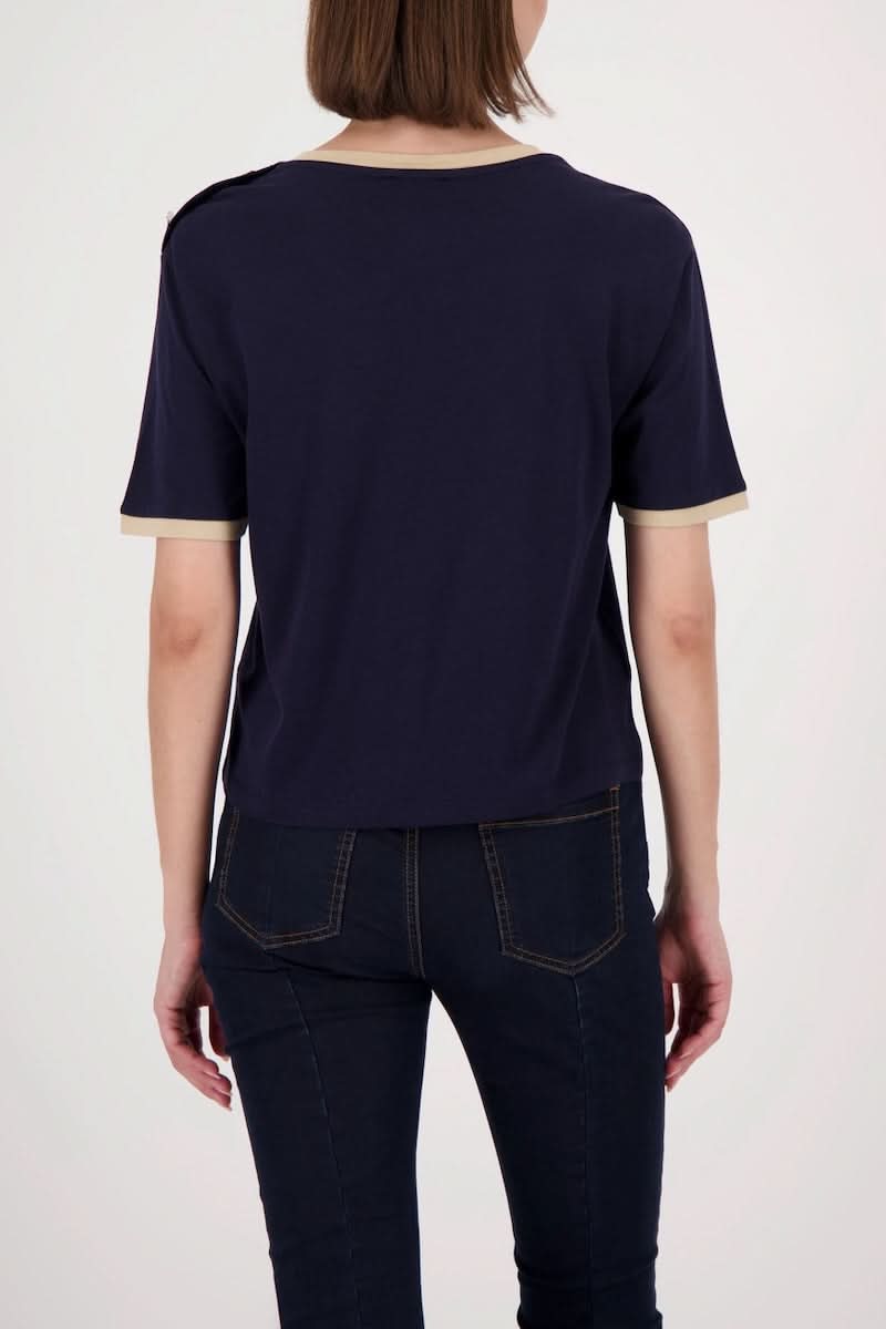 Femme portant un T-shirt à boutons décoratifs sur l’épaule, couleur marine, avec bordures contrastantes, vue de dos.