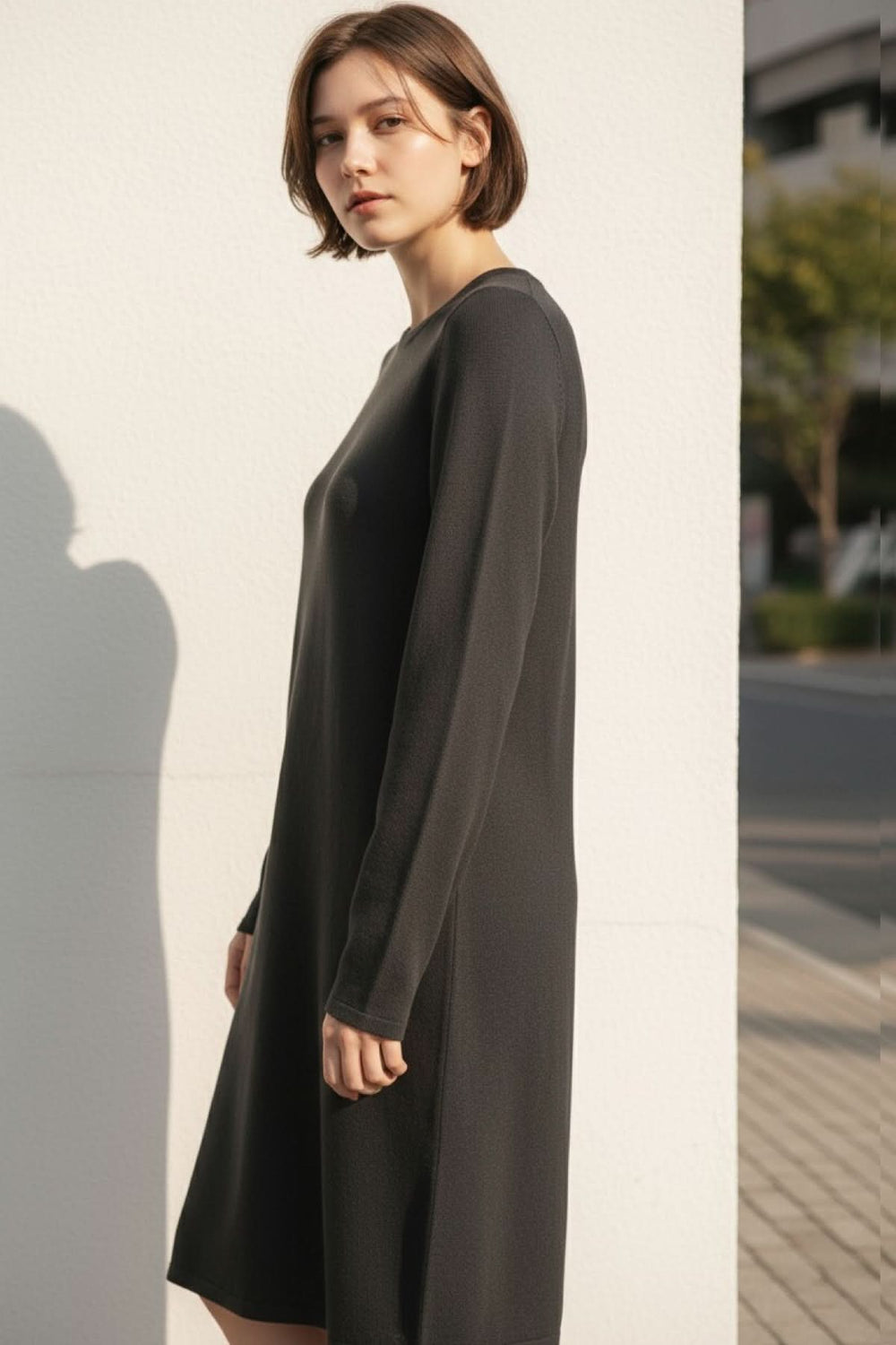 Femme portant une robe de tricot noire à manches longues avec encolure ronde et coupe fluide.