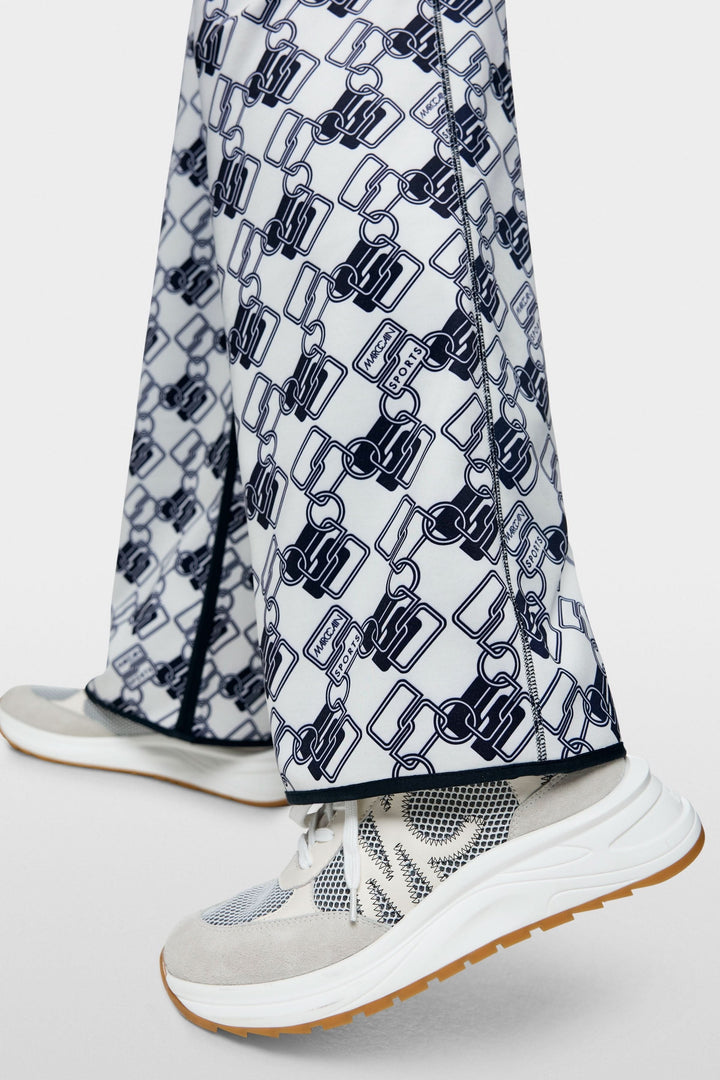 Pantalon de jogging réversible Washington avec motif graphique maillons entrelacés, porté avec des baskets sportives.