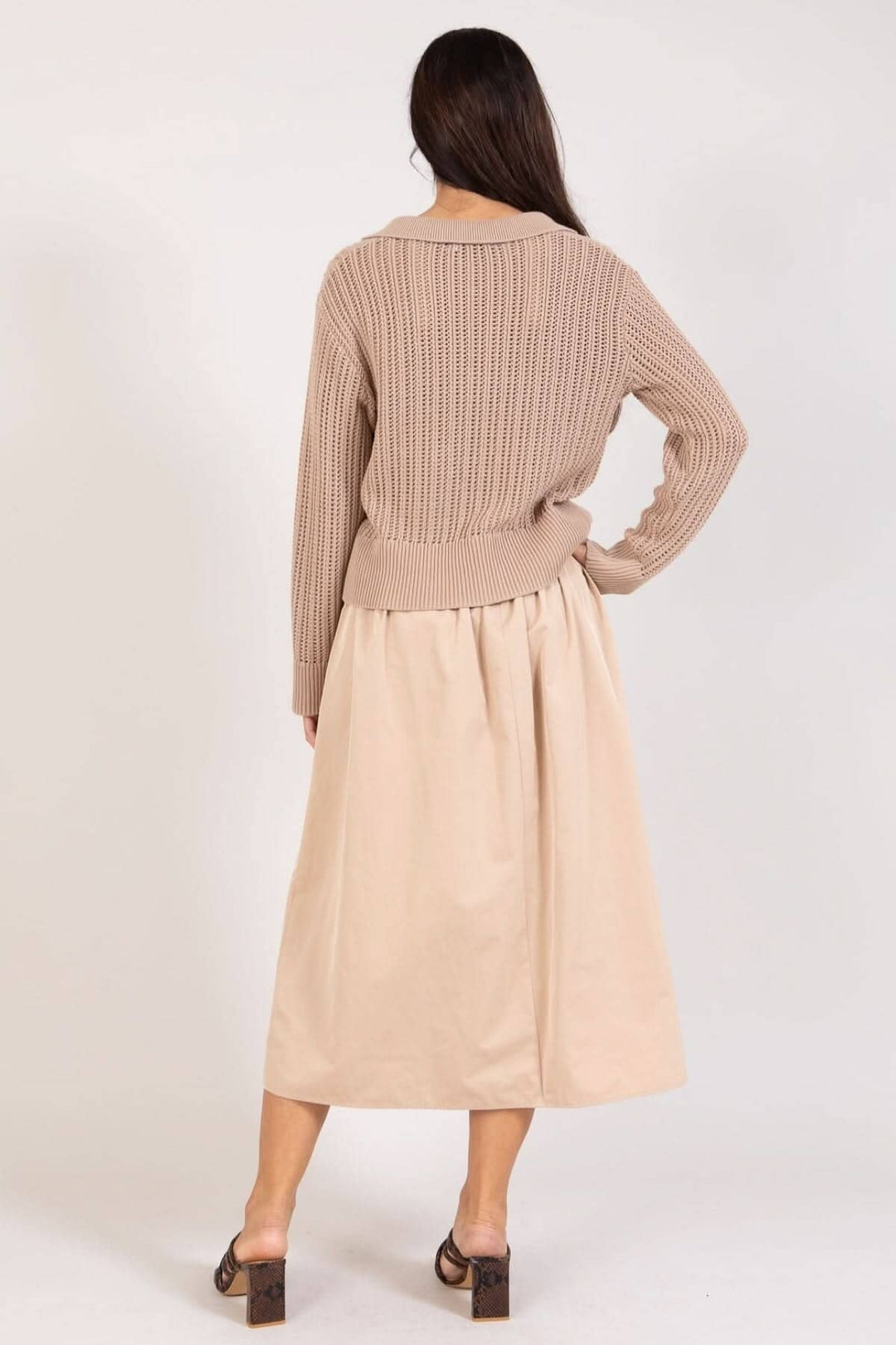 Femme vue de dos portant un chandail maille ouverte beige et une jupe beige au-dessous des genoux.