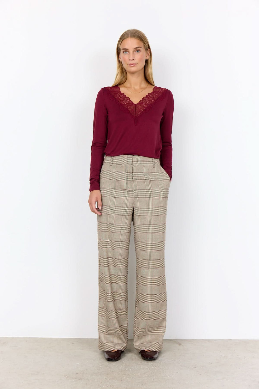 Femme portant un pantalon à carreaux prince-de-galles avec une blouse rouge élégante, style moderne et confortable.