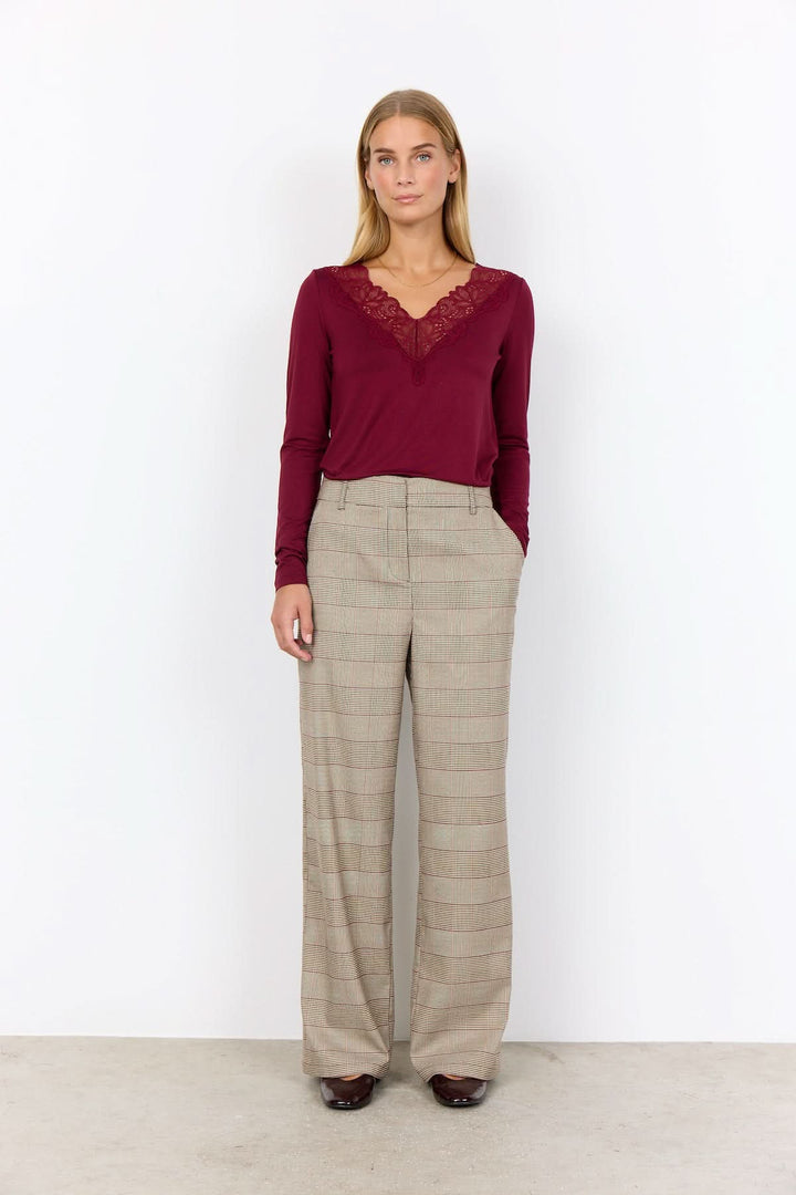 Femme portant un pantalon à carreaux prince-de-galles avec une blouse rouge élégante, style moderne et confortable.