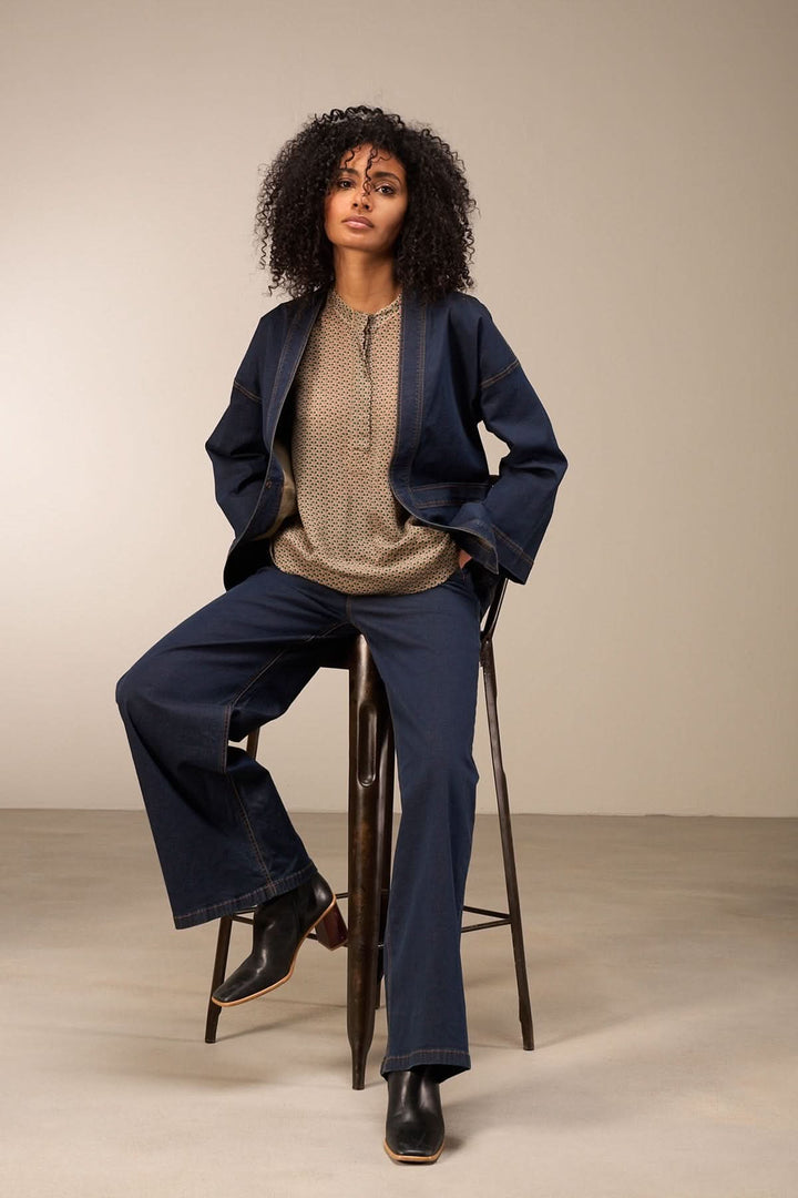 Femme portant un jean coupe large, haut texturé et blazer, assise sur une chaise en métal.