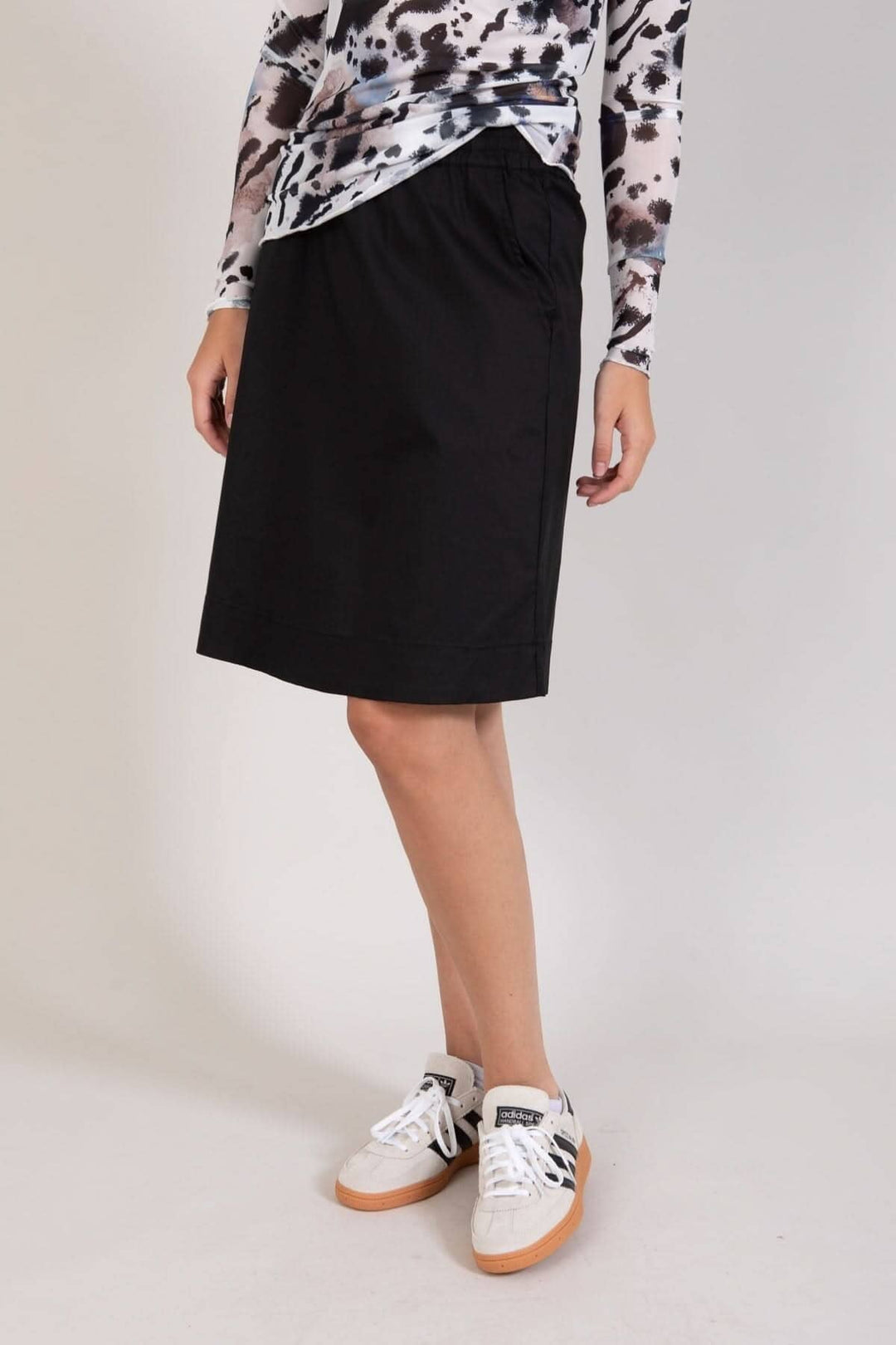 Jupe courte noire évasée jusqu'aux genoux avec poches et taille élastique, portée avec des sneakers blanches.