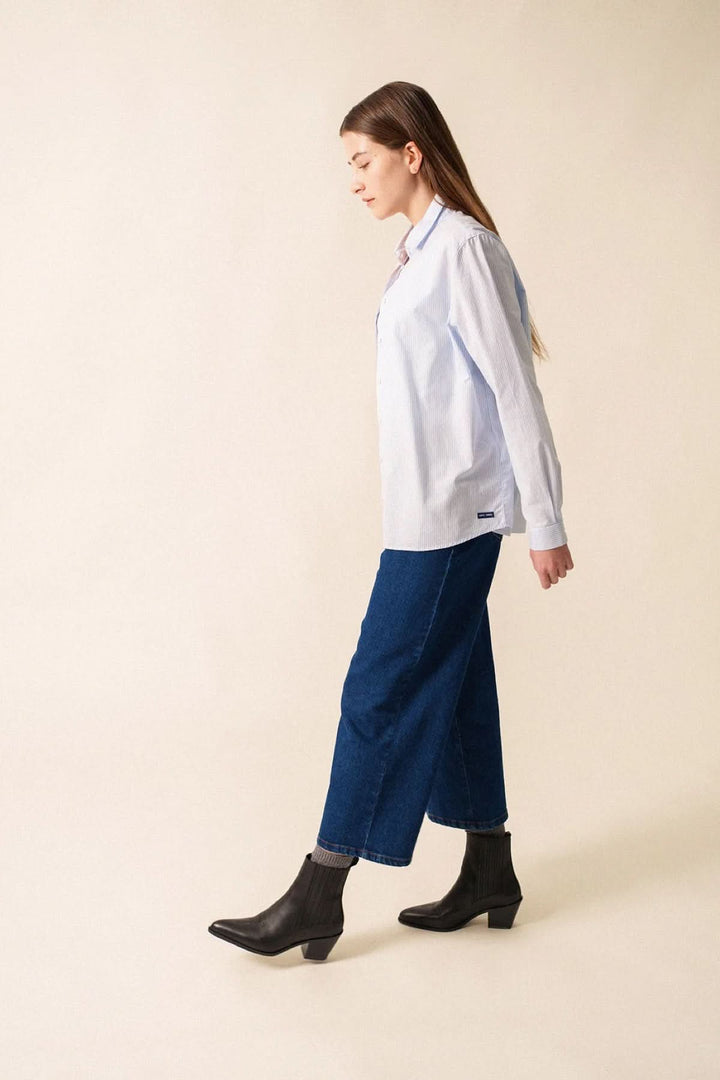 Femme portant une chemise rayée Léna en coton avec un pantalon en denim, marchant avec élégance.