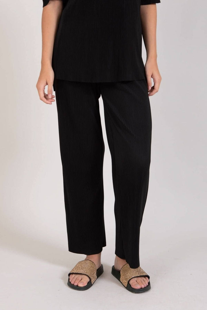 Pantalon ample noir à motif de lignes, taille élastique et poches avant, porté avec des sandales.