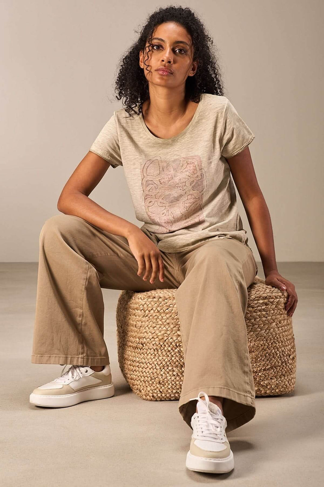 T-shirt imprimé artistique porté avec un pantalon beige et des chaussures blanches, style décontracté.