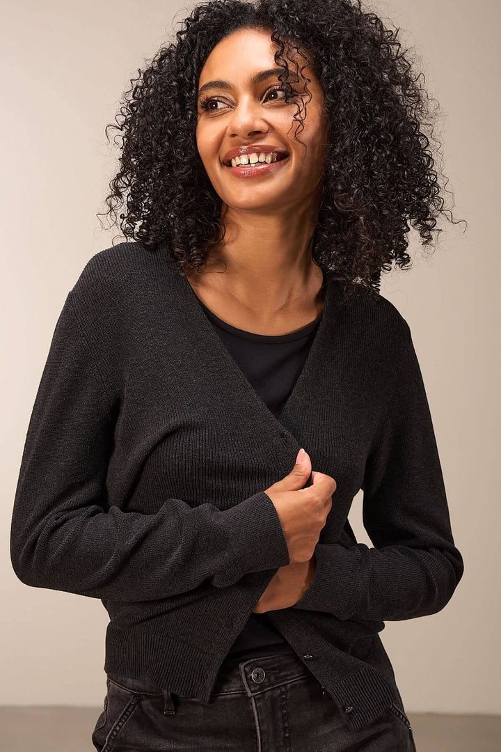 Femme souriante portant un cardigan simple à manches longues, encolure V, couleur noir.